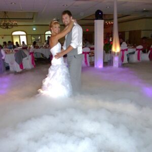 A bride and groom standing in a cloud of smoke created by DJ equipment.