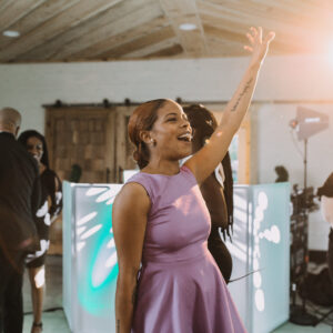 A woman is waving her arms in the air at a wedding reception.