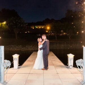 A bride and groom standing on a dock with sparklers.