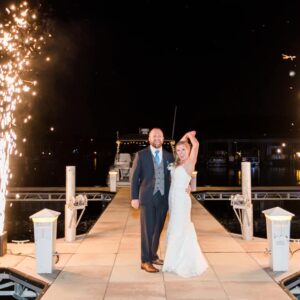 A bride and groom standing on a dock with sparklers.