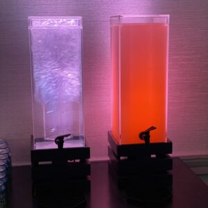 Two drink dispensers on a table next to each other.