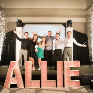 A group of people posing in front of a sign that says allie.