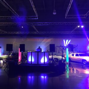 A school dance featuring a DJ set up in a room with a lot of cars.