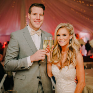 A bride and groom holding champagne glasses in a tent at their Georgia corporate DJ event.