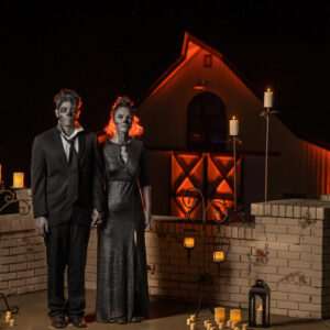 A couple dressed as zombies stand in front of a barn at night, awaiting the arrival of their Georgia wedding DJ.