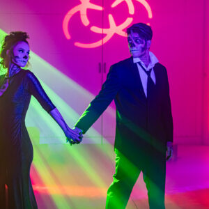 A man and woman holding hands in a dark room, illuminated softly by the ambient lighting of a photo booth rental in Georgia.