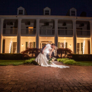 A bride and groom kissing in front of a large white house at night, with a Georgia corporate DJ providing background music.