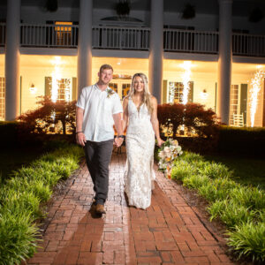 A bride and groom standing in front of a white house at night, ready for their Georgia wedding DJ to start the evening's entertainment.