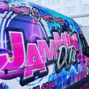 A van with a pink and purple design, advertising a DJ service, parked in front of a building.