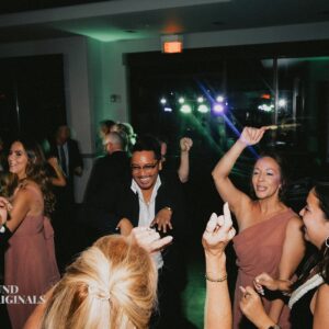 People dancing and enjoying themselves at a lively wedding, with colorful lights illuminating the background.