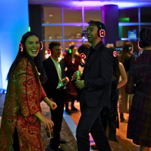 In a dimly lit room aglow with colorful lights, people sway and groove to their own rhythm at a Silent Disco. Each dancer, immersed in personal melodies flowing through their headphones, creates an atmosphere alive with invisible energy.