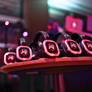 A row of black and red wireless headphones sits on a round table in a dimly lit room, ready to kick off the ultimate silent disco experience.