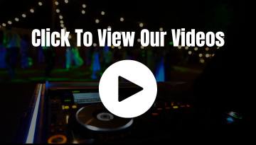 The DJ booth, illuminated by a play button overlay, invites you to click and explore our videos. Against a dark backdrop adorned with string lights, "Click To View Our Videos" sets the stage for JAMMIN' DJs' premium entertainment experience.
