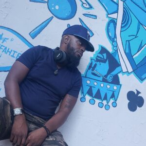 Man in a blue shirt, hat, and headphones leans against a wall with blue graffiti art, embodying the cool confidence of professional DJs.