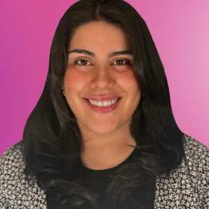 A person with long dark hair smiles at the camera, wearing a patterned top over a black shirt, in front of a pink gradient background—capturing the upbeat energy often seen in professional DJs.