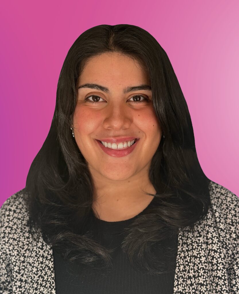 A person with long dark hair smiles at the camera, wearing a patterned top over a black shirt, in front of a pink gradient background—capturing the upbeat energy often seen in professional DJs.